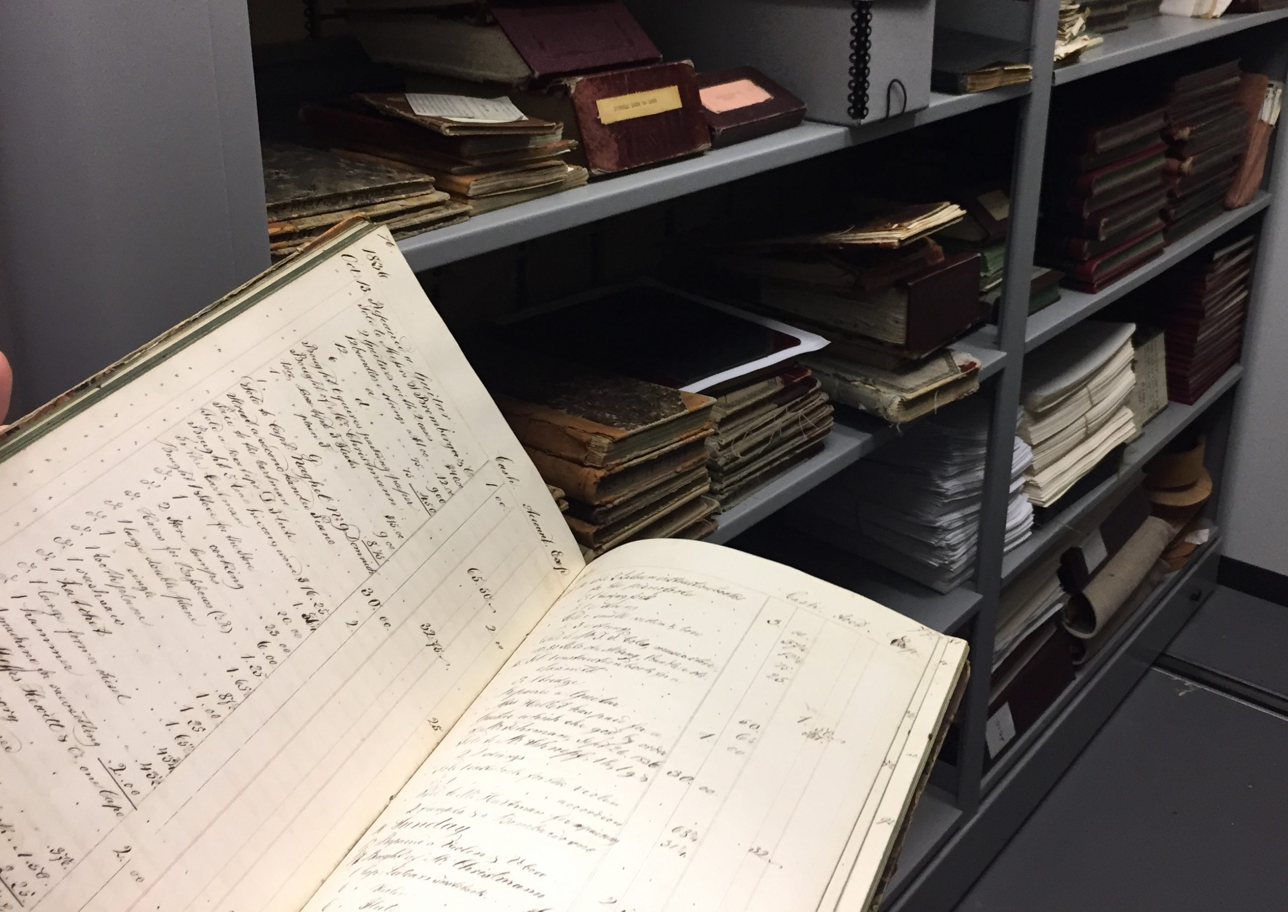 15 martin ledger An opened ledger book from 1836 with archive stacks in the background.