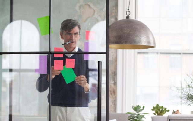 Ed Rodley arranging post it notes on a glass wall with a sharpie pen in his mouth