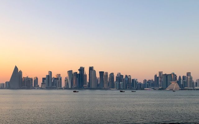 Part of Doha skyline at dusk. With blue and orange sky, buildings, and water in the foreground