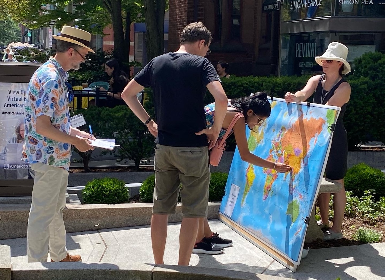 putting pin in the map Annie holding large map of the world with people placing pins in the places their family is from